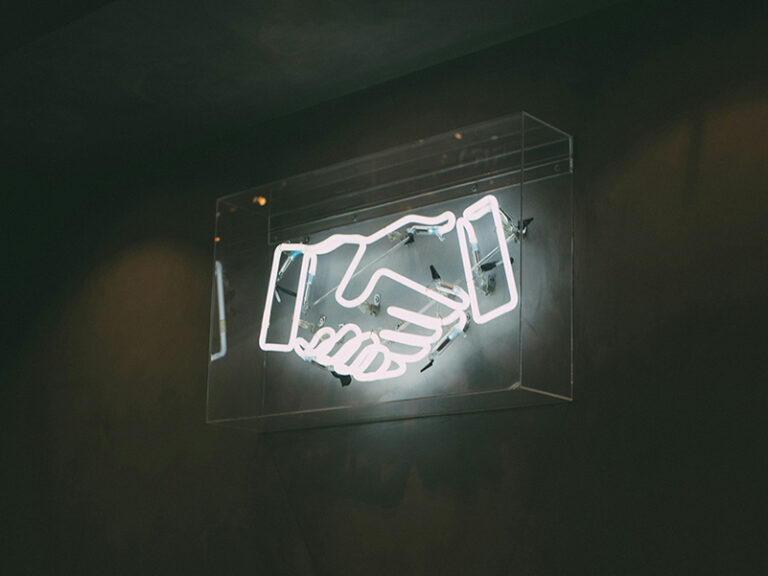 Lichtreclame met twee handen die elkaar schudden. Illustreert de samenwerking tussen domoticabedrijf Comfortica en Slimmer Wonen.