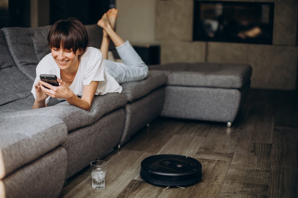 vrouw ligt op bank terwil robotstofzuiger stofzuigt