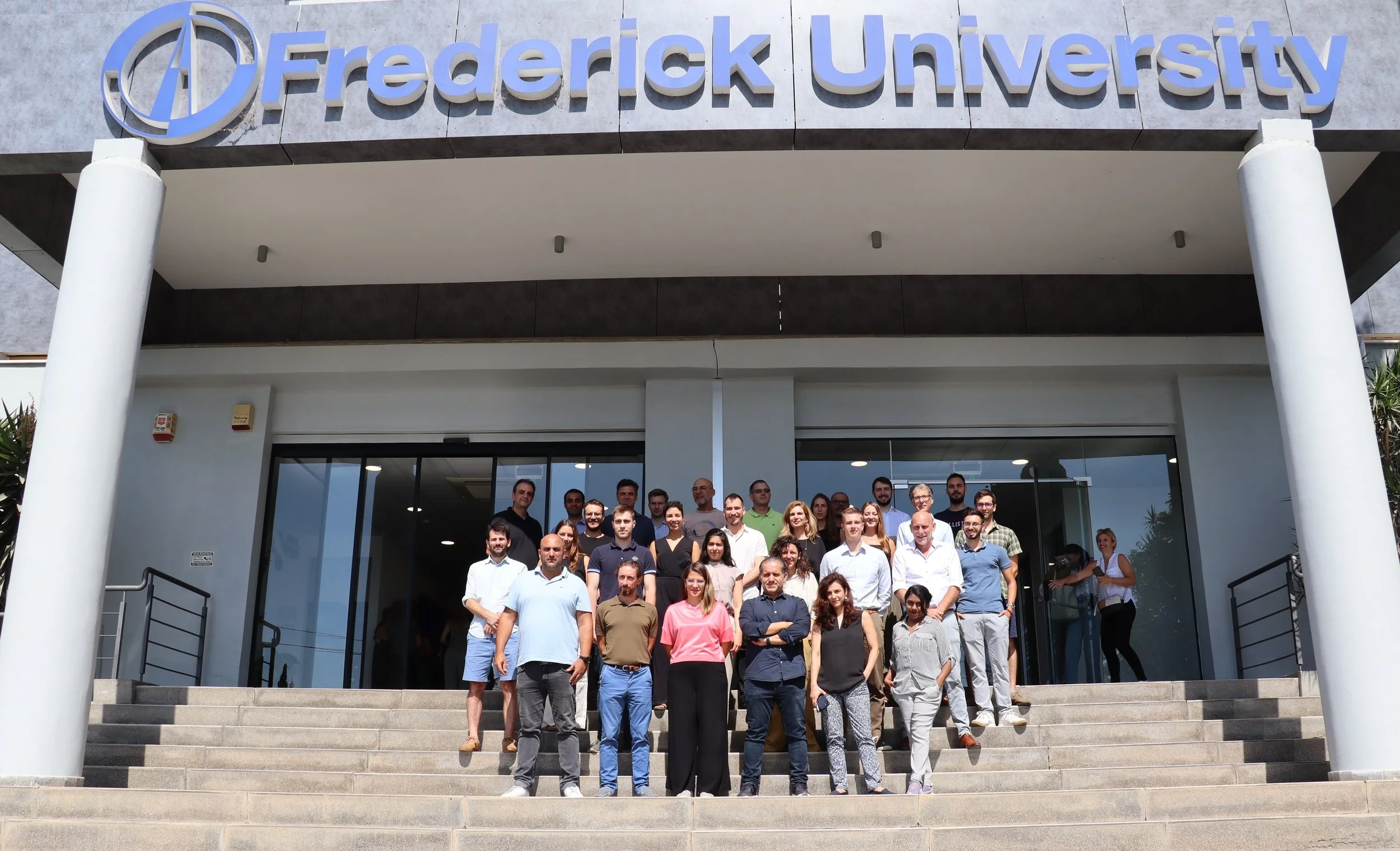 Groepsfoto van de 22 partijen die vormgeven aan het INBLANC EU project duurzaam wonen en werken. Op de grijze entree trappen van de Frederick University in Cyprus.