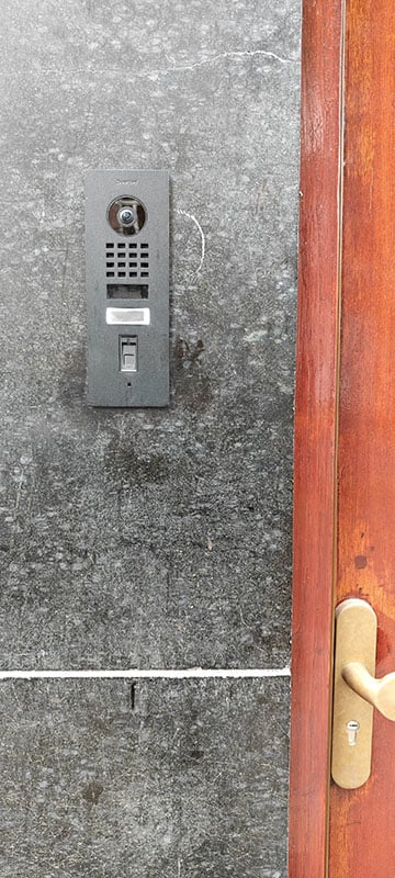 Doorbird intercom met fingerprint reader op zwart marmeren tegels rondom rood eikenhouten deur van een Amsterdamse pijpenla woning.