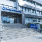 Grijs gebouw van de Frederick University op Cyprus. Voor de ingang met vier glazen deuren een brede trap bestaande uit 13 treden. Deel van het EU project INBLANC duurzaam wonen en werken waaraan Comfortica deelneemt.