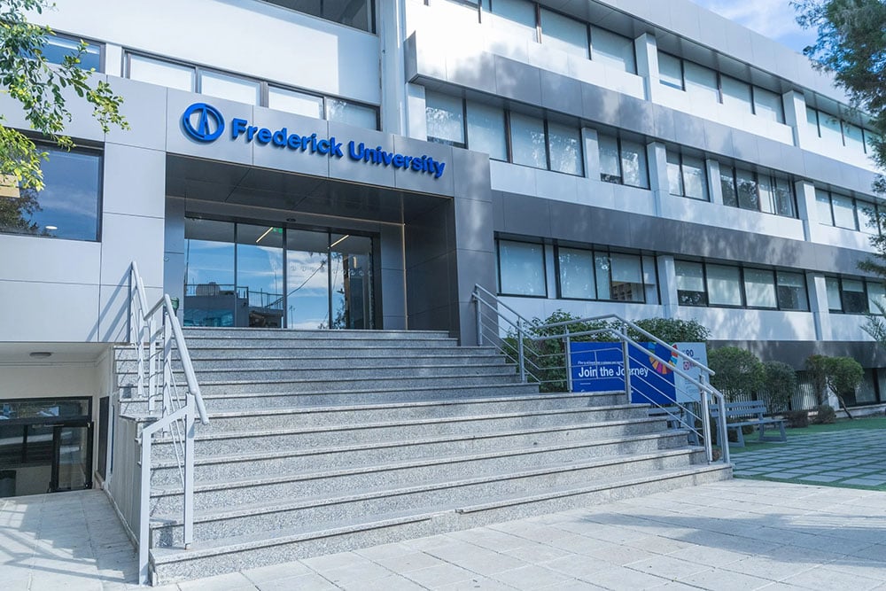 Grijs gebouw van de Frederick University op Cyprus. Voor de ingang met vier glazen deuren een brede trap bestaande uit 13 treden. Deel van het EU project INBLANC duurzaam wonen en werken waaraan Comfortica deelneemt.